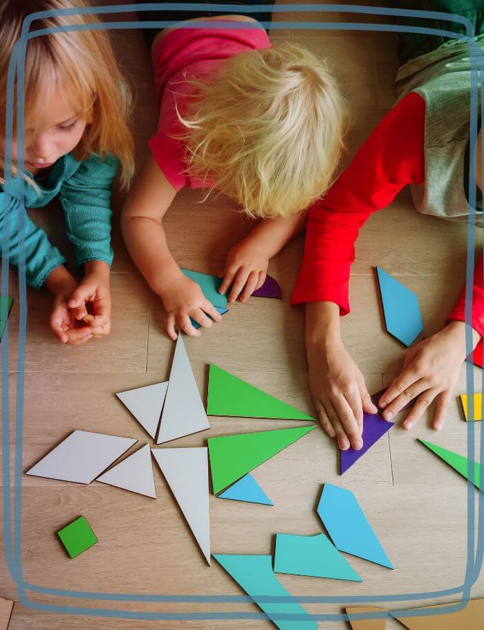 3 young students playing with tanagram shapes on the floor