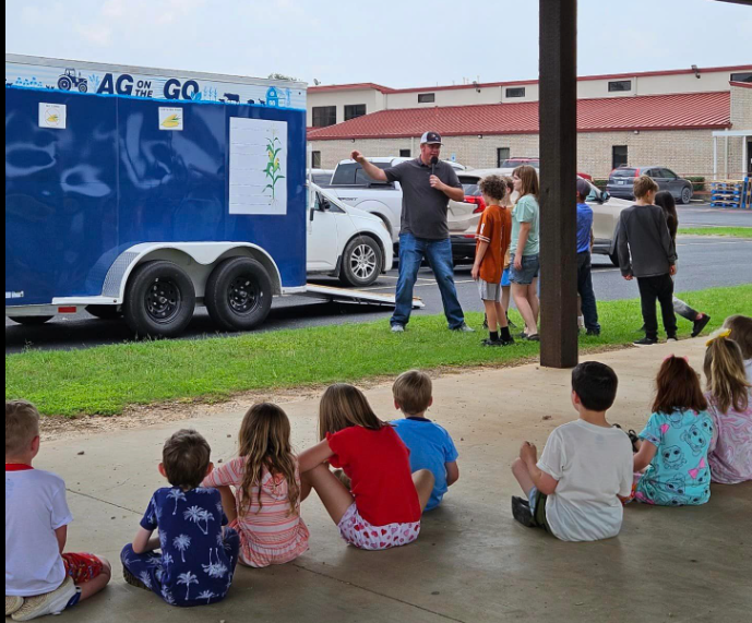 Image of man giving presentation in front of agriculture trailer for elementary students